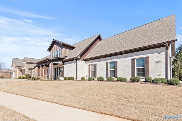 craftsman inspired home featuring a shingled roof, brick siding, and a front lawn