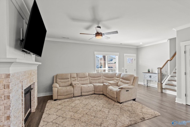 living room featuring dark wood finished floors, crown molding, a brick fireplace, baseboards, and stairs