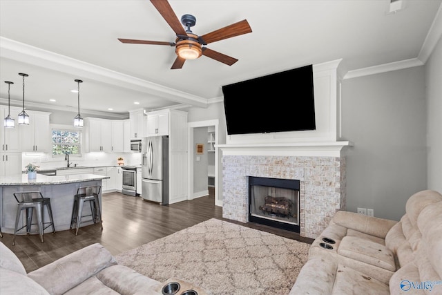 living room with ornamental molding, ceiling fan, dark wood-type flooring, and a fireplace with flush hearth