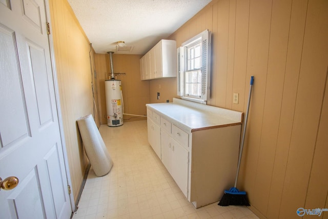 laundry area featuring water heater, a textured ceiling, cabinets, and wood walls