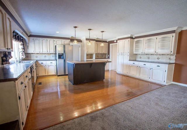 kitchen with sink, stainless steel fridge, hanging light fixtures, ornamental molding, and a kitchen island