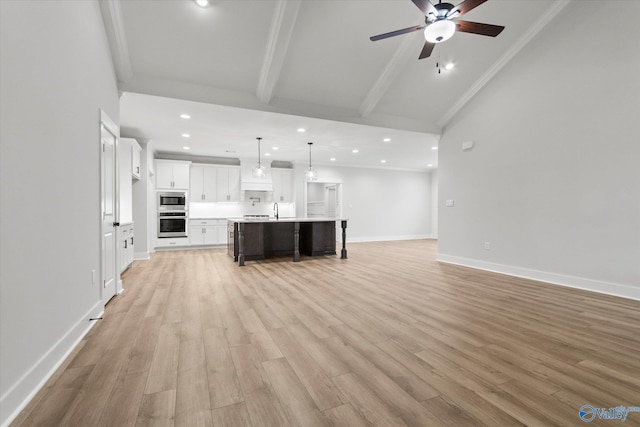 unfurnished living room featuring ceiling fan, sink, lofted ceiling with beams, and light hardwood / wood-style flooring