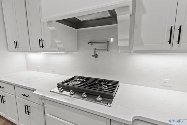 kitchen featuring light stone counters, white cabinetry, backsplash, and gas cooktop