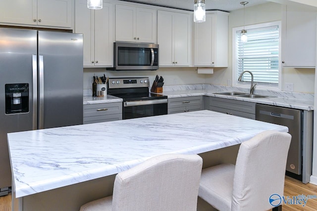 1409 8th Ave SE, Decatur, AL 35601 - kitchen featuring appliances with stainless steel finishes, a sink, light wood-style flooring, decorative light fixtures, and a breakfast bar