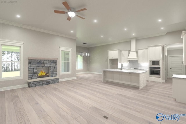 kitchen with white cabinets, a stone fireplace, hanging light fixtures, a kitchen island with sink, and oven