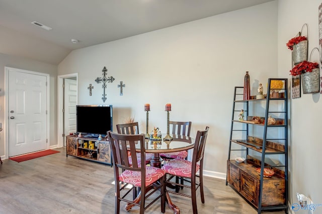 dining space featuring visible vents, baseboards, wood finished floors, and vaulted ceiling