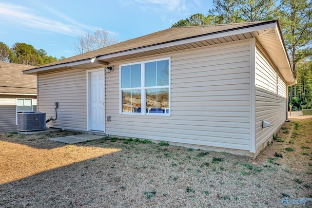 rear view of property featuring central air condition unit and a lawn