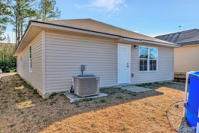 rear view of property with a yard, central AC, and a shingled roof