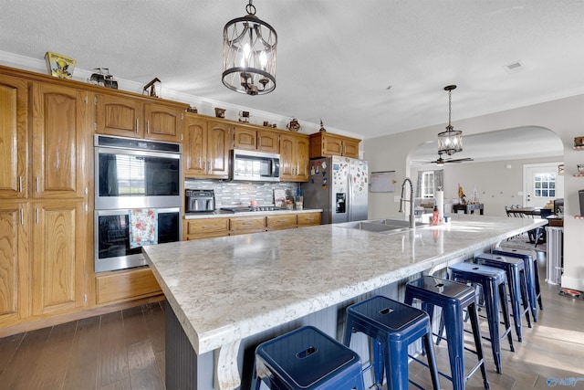 kitchen with dark hardwood / wood-style flooring, ceiling fan with notable chandelier, stainless steel appliances, a large island with sink, and decorative light fixtures