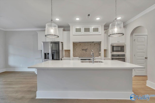 kitchen featuring ornamental molding, light countertops, stainless steel appliances, arched walkways, and a sink