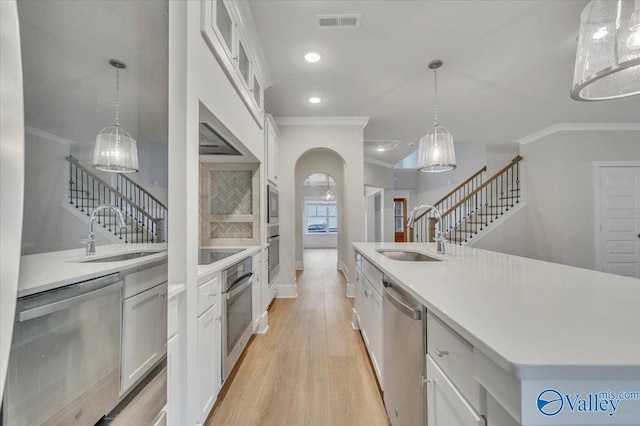 kitchen with light wood-style flooring, a sink, ornamental molding, and stainless steel appliances