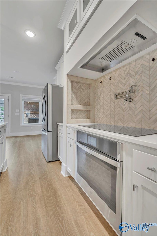 kitchen featuring stainless steel appliances, white cabinets, wall chimney exhaust hood, and light countertops