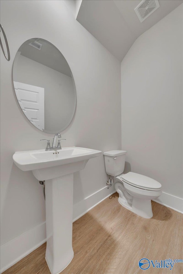 half bath featuring toilet, wood finished floors, baseboards, and visible vents