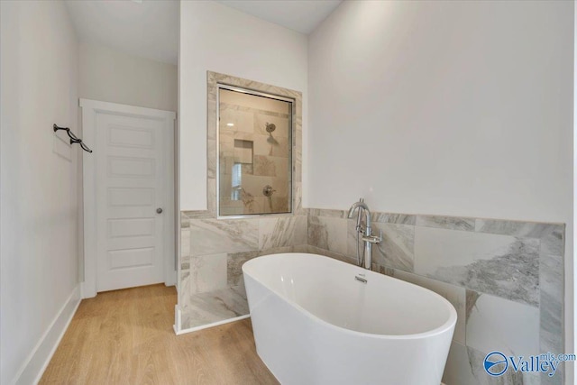 bathroom featuring a freestanding tub, tile walls, tiled shower, and wood finished floors
