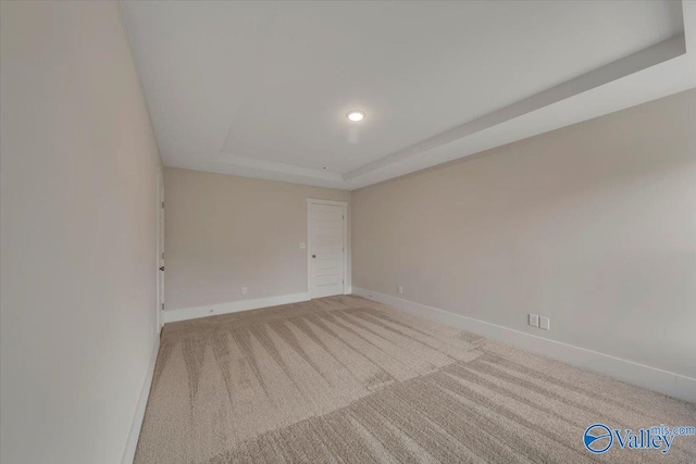 empty room with baseboards, a raised ceiling, and light colored carpet