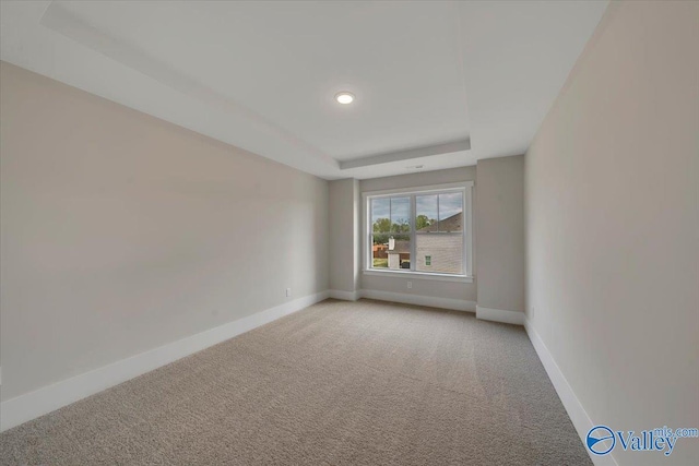 empty room featuring a raised ceiling, light carpet, and baseboards