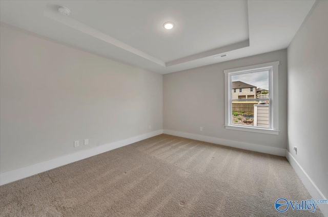spare room featuring a tray ceiling, visible vents, baseboards, and carpet