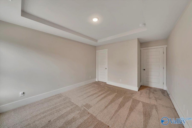 empty room featuring carpet, baseboards, and a raised ceiling