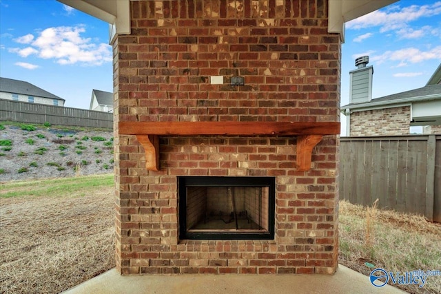 exterior details featuring brick siding, fence, and a brick fireplace