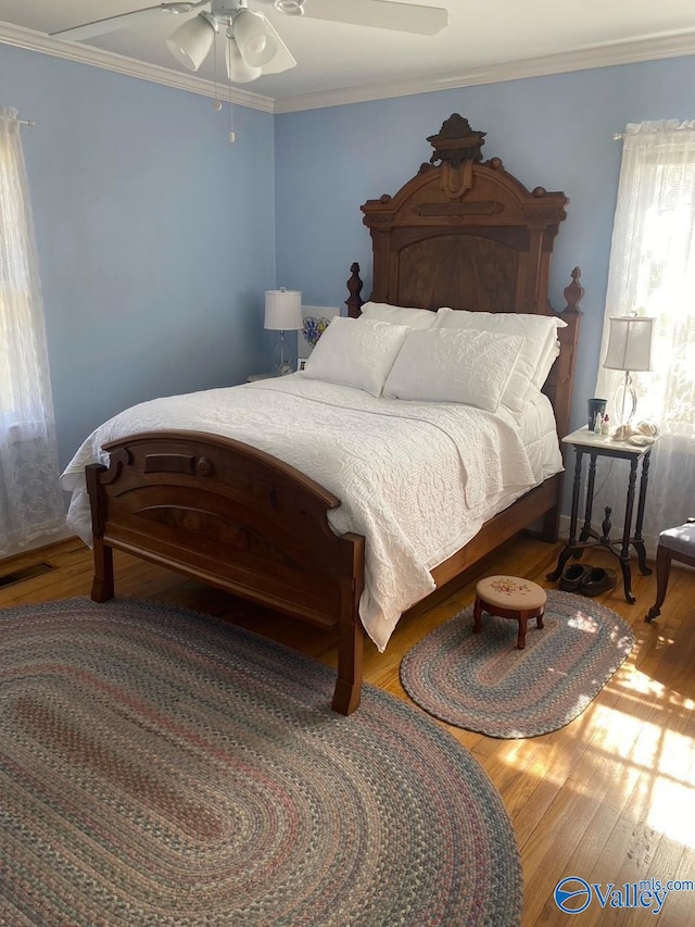 bedroom featuring ceiling fan, ornamental molding, visible vents, and wood finished floors
