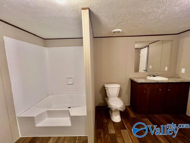 bathroom with hardwood / wood-style floors, toilet, a bath, vanity, and a textured ceiling