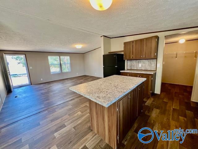 kitchen with a textured ceiling, a kitchen island, dark hardwood / wood-style floors, tasteful backsplash, and black fridge