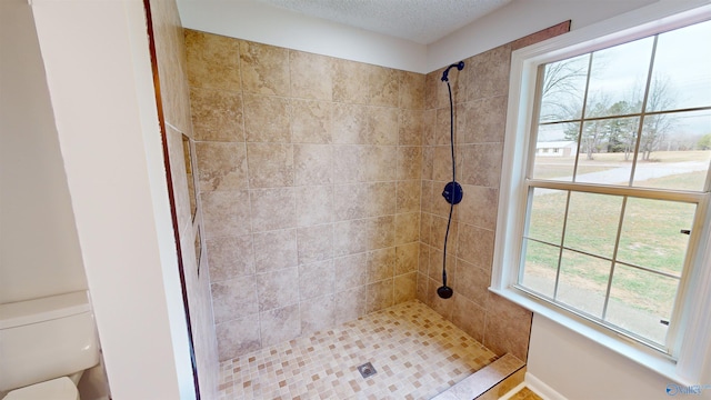 bathroom featuring tiled shower, toilet, and a textured ceiling