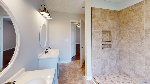 bathroom featuring ceiling fan, vanity, a textured ceiling, and a tile shower