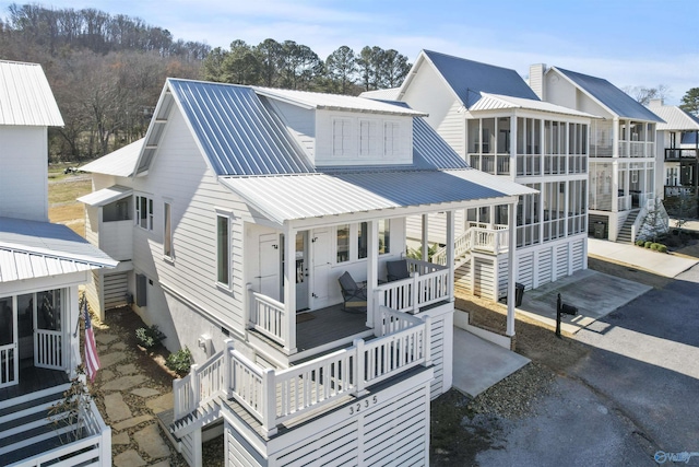 rear view of house with a porch, a sunroom, metal roof, and stairs