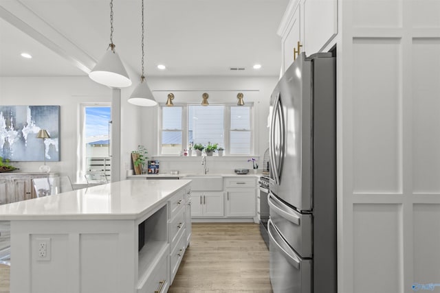 kitchen featuring a center island, stainless steel appliances, light countertops, hanging light fixtures, and white cabinets