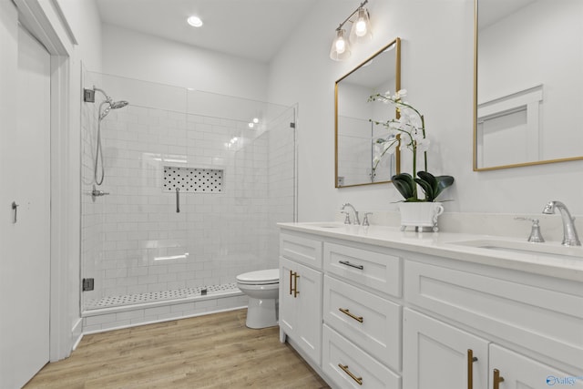 bathroom featuring double vanity, toilet, a stall shower, a sink, and wood finished floors