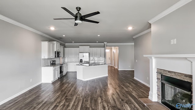 kitchen with decorative backsplash, appliances with stainless steel finishes, white cabinets, a stone fireplace, and an island with sink