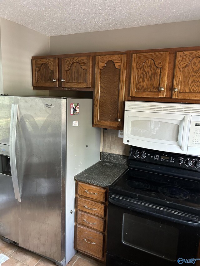 kitchen with stainless steel refrigerator with ice dispenser, black electric range oven, white microwave, light tile patterned floors, and a textured ceiling