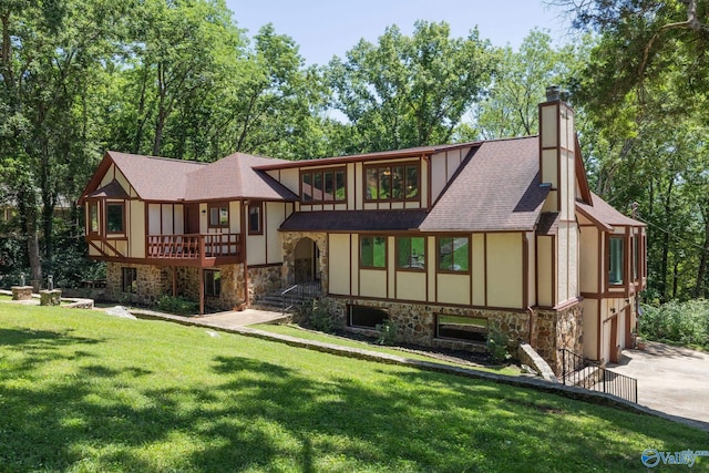 rear view of house featuring roof with shingles, a chimney, stucco siding, stone siding, and a lawn