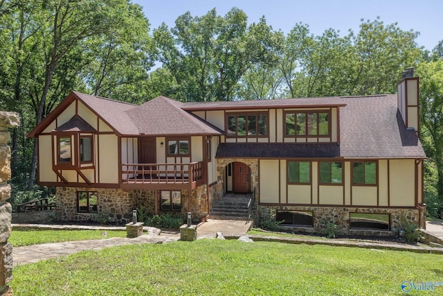 english style home with stone siding, stucco siding, a chimney, and a front lawn