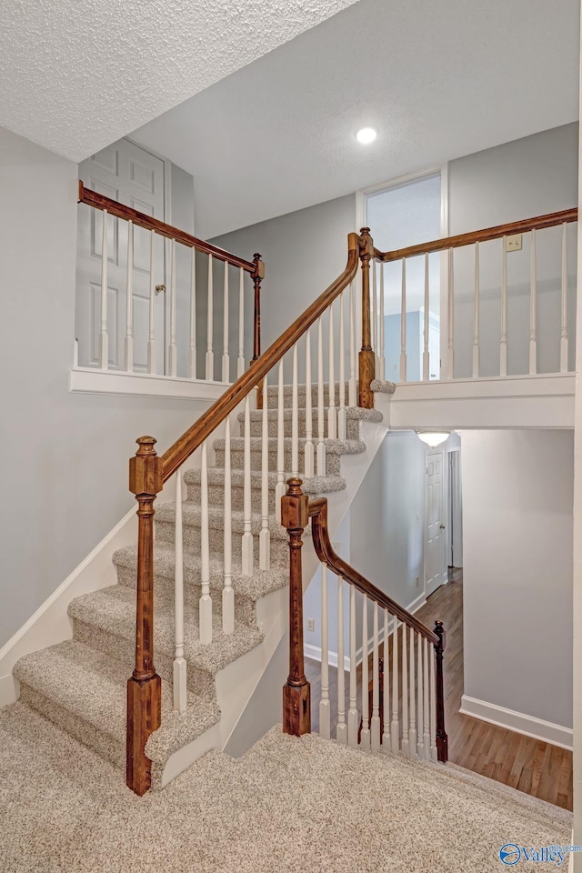 staircase featuring a textured ceiling, baseboards, and wood finished floors