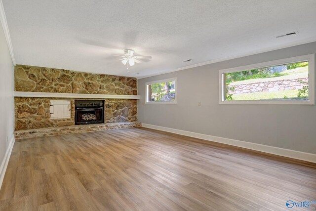 unfurnished living room with wood finished floors, baseboards, visible vents, a stone fireplace, and a textured ceiling