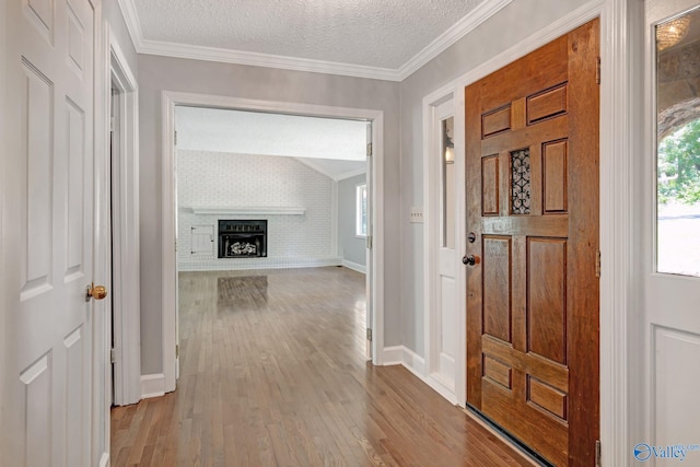 entrance foyer featuring crown molding, baseboards, a fireplace, wood finished floors, and a textured ceiling