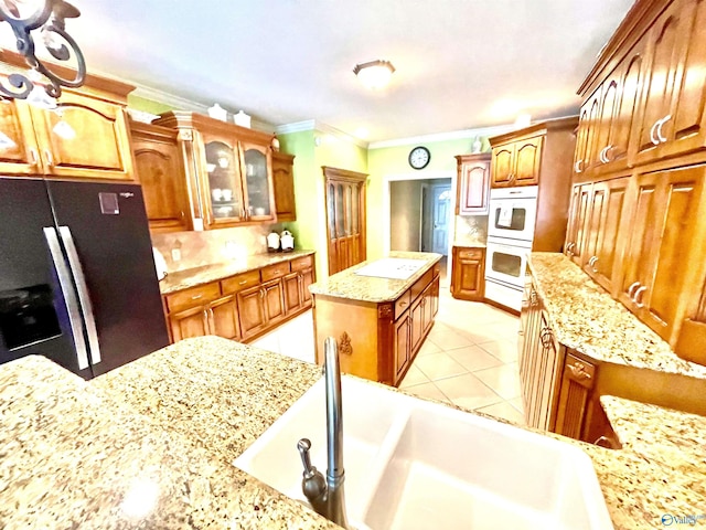 kitchen with black fridge, sink, ornamental molding, double oven, and light stone countertops