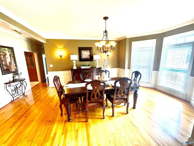 dining space with ornamental molding, an inviting chandelier, and light hardwood / wood-style floors