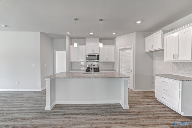 kitchen featuring a center island with sink, stainless steel microwave, white cabinets, and a sink