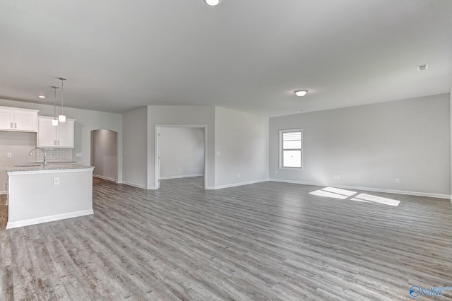 unfurnished living room featuring light wood-style flooring, visible vents, arched walkways, and baseboards