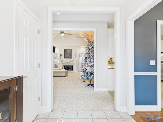 hall featuring baseboards, lofted ceiling, and light colored carpet