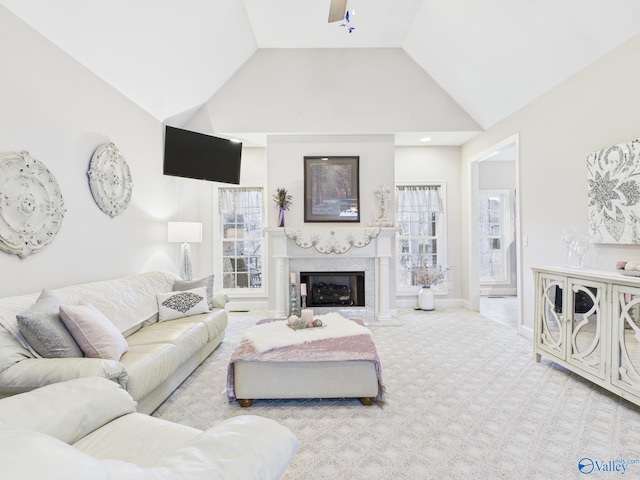 living room with high vaulted ceiling, carpet floors, a premium fireplace, a ceiling fan, and baseboards