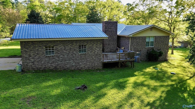 back of house with cooling unit, a yard, a chimney, metal roof, and brick siding