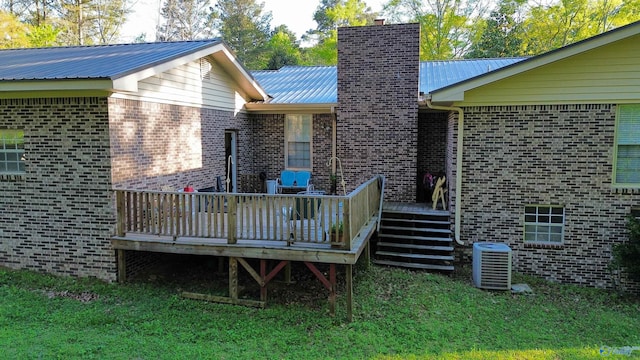 back of property with a chimney, brick siding, metal roof, central air condition unit, and a wooden deck