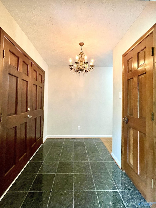 foyer entrance featuring baseboards, a chandelier, a textured ceiling, and dark tile patterned floors