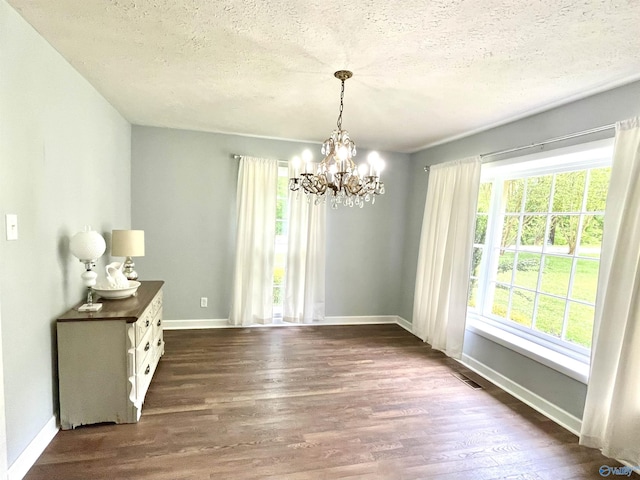 unfurnished dining area with dark wood-style flooring, a textured ceiling, a notable chandelier, and baseboards