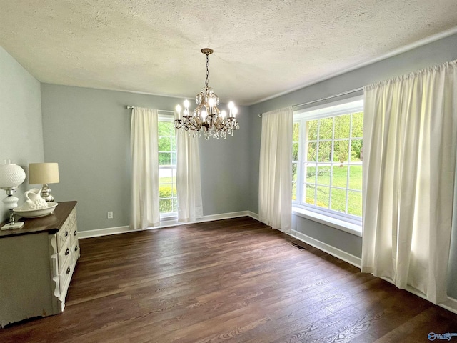 unfurnished dining area with a chandelier, a textured ceiling, dark wood-style flooring, and baseboards