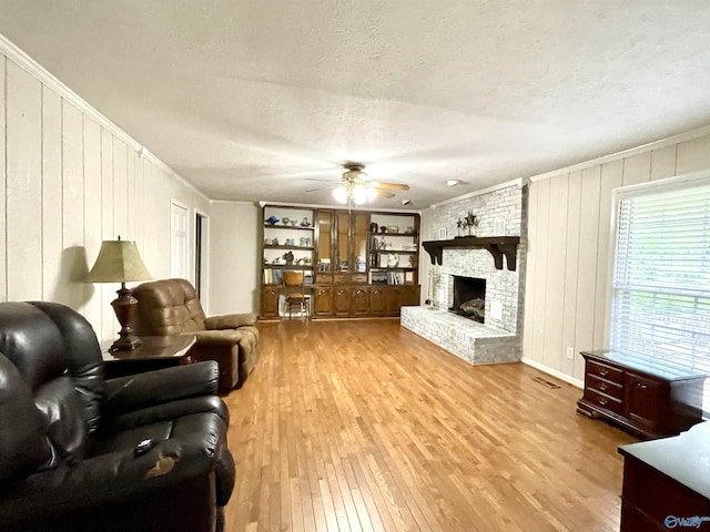 living area with wood finished floors, crown molding, a textured ceiling, ceiling fan, and a large fireplace